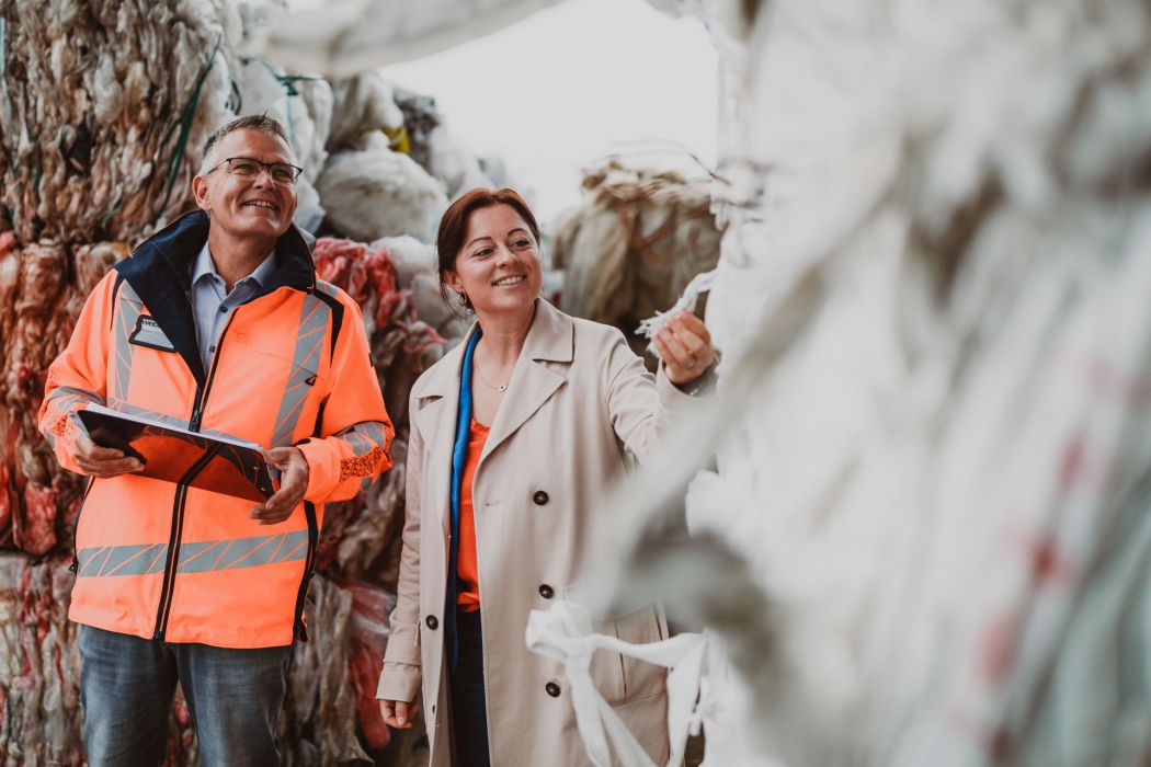 Weber Team zwischen gepressten Folien und Kartonagen. Ein freundlicher Mann und eine lachende Frau vom Weber Team stehen zwischen gepressten Folien und Kartonagen und prüfen in ihrer Hand die Materialien.